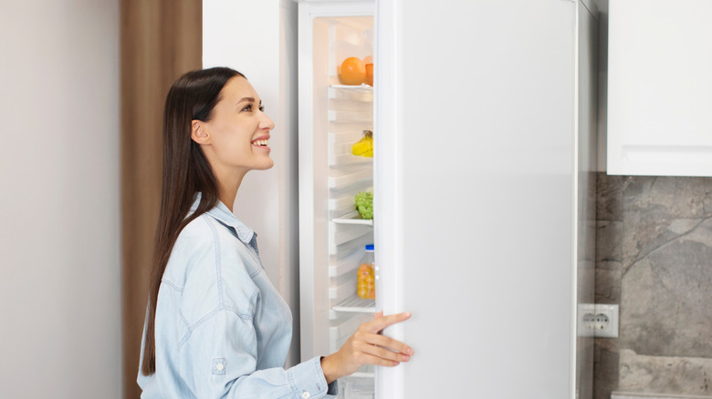 Lady looking inside of fridge while standing in kitchen, opening refrigerator and searching for food.
