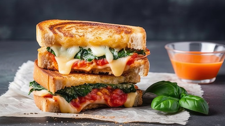 Grilled cheese sandwich with spinach and tomato next to basil and tomato soup.