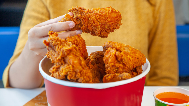 hand holding fried chicken over bucket