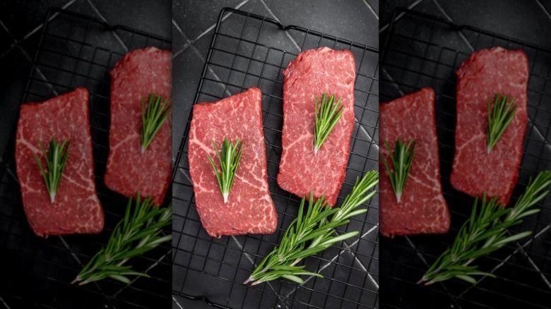 raw steaks on a metal rack with a bunch of herbs dumped all over the place