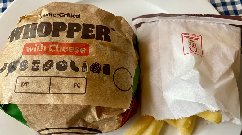 A Burger King Whopper resting on a white fast food wrapper with fries