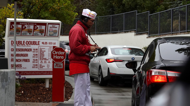 An In-N-Out employee taking drive-thru orders outdoors