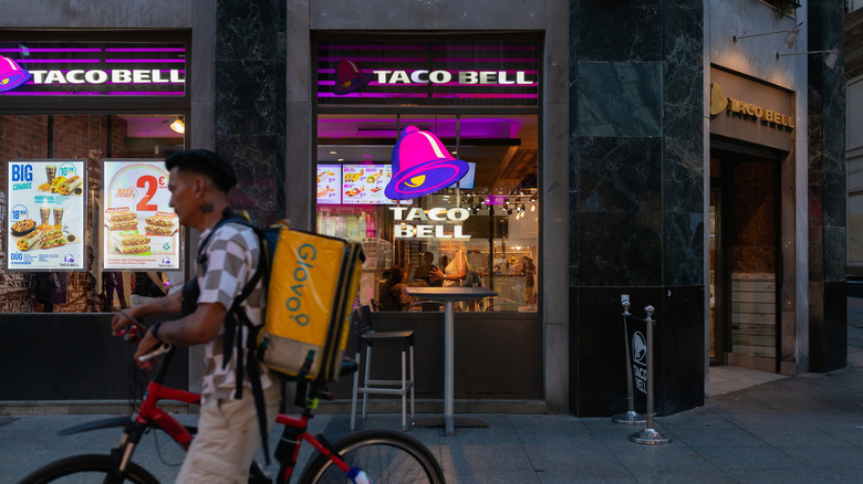 A man riding a bike in front of a Taco Bell.