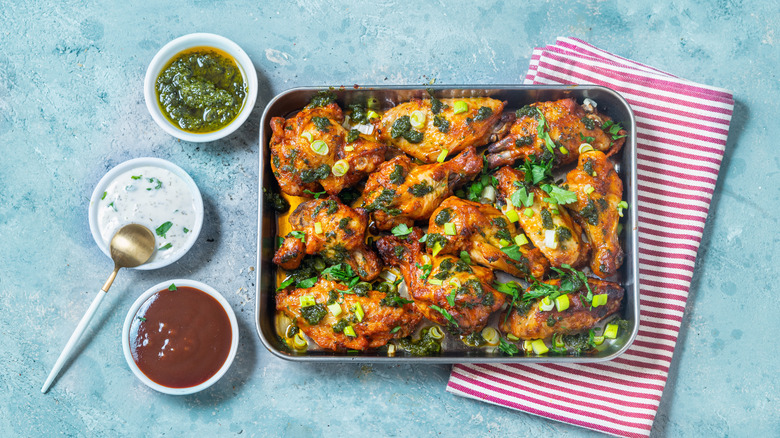 Grilled chicken in pan with herbs and green salsa, alongside three sauces