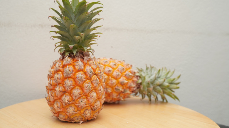 Two ripe, whole pineapples on top of a circular, wooden table.