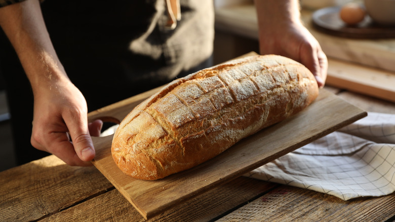 hands hold loaf of homemade bread on wooden slab