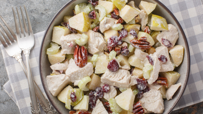 A bowl of SugarBee apple chicken salad on a gray and white gingham napkin with two forks next to it