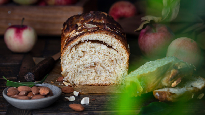 A sliced loaf of SugarBeen apple cinnamon babka on a wooden table with apples and pecans