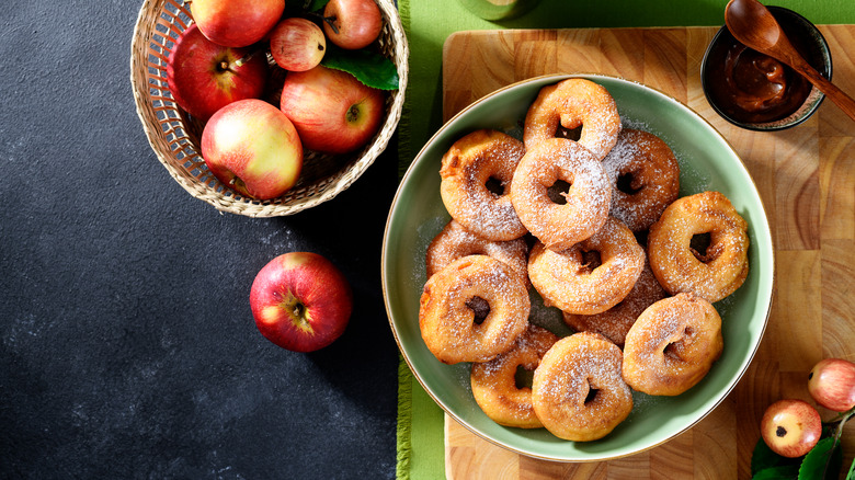 A large green plate of SugarBee apple donuts sits on a wooden cutting board next to a wicker bowl of SugarBee apples