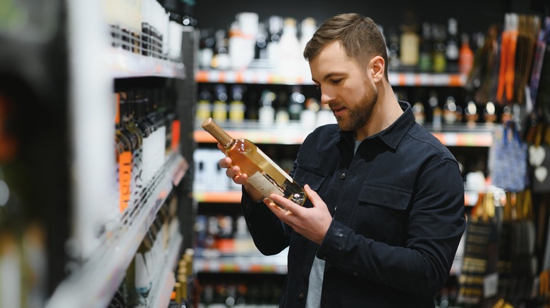 Man looks at wine label in grocery store wine aisle