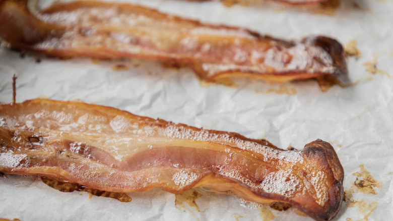 Two crispy strips of cooked bacon on a lined baking sheet