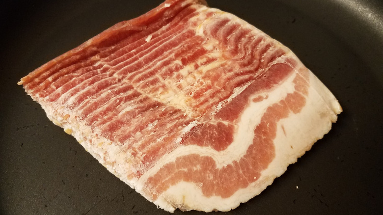 Raw strips of frozen bacon stuck together in a skillet