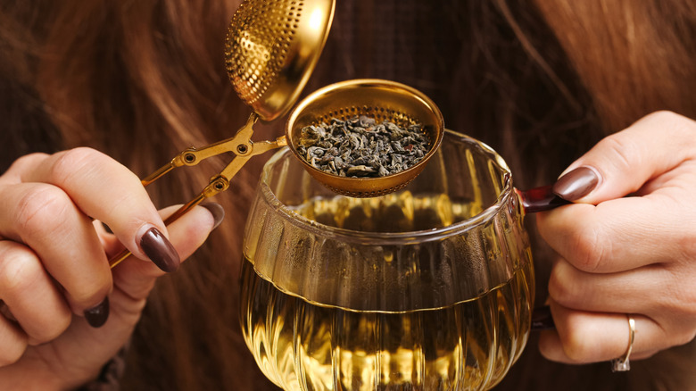 Person holding a tea strainer filled with loose tea above a cup of tea