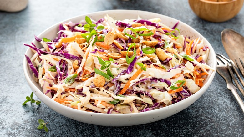 Coleslaw in white bowl with utensils nearby