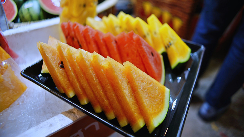 Close-up of triangular slices of orange, red, and yellow watermelon on a black tray