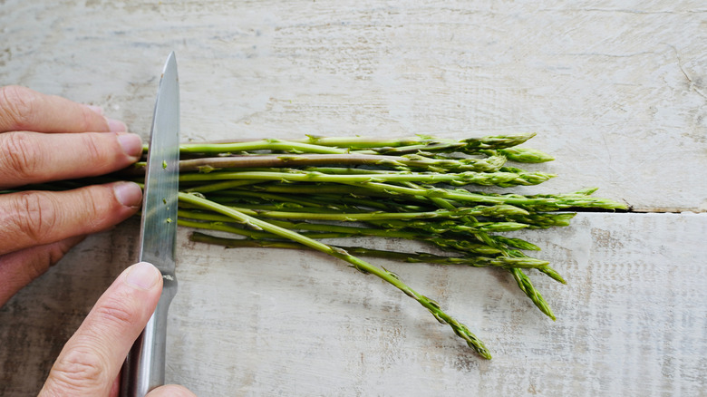 A person cutting thin raw asparagus spears with a knife