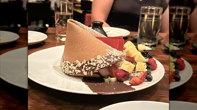 A large fortune cookie sitting on a plate with fruit and melted chocolate