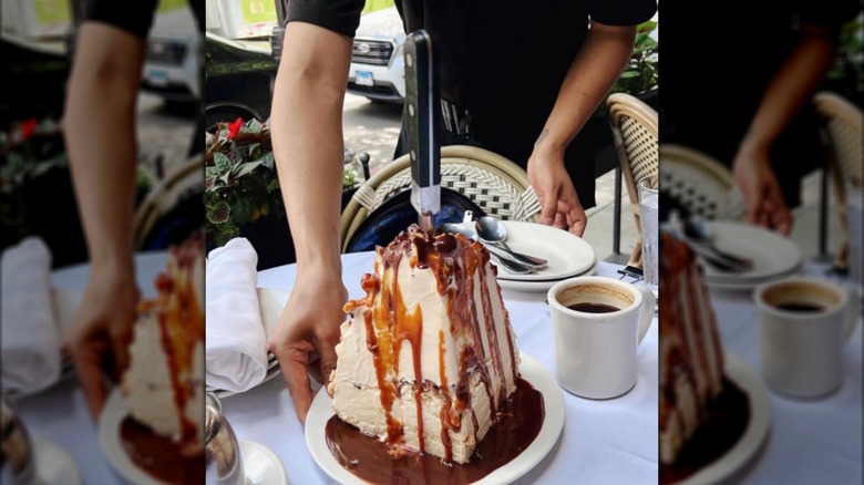 A server presenting a slive of ice cream pie covered in caramel sauce.