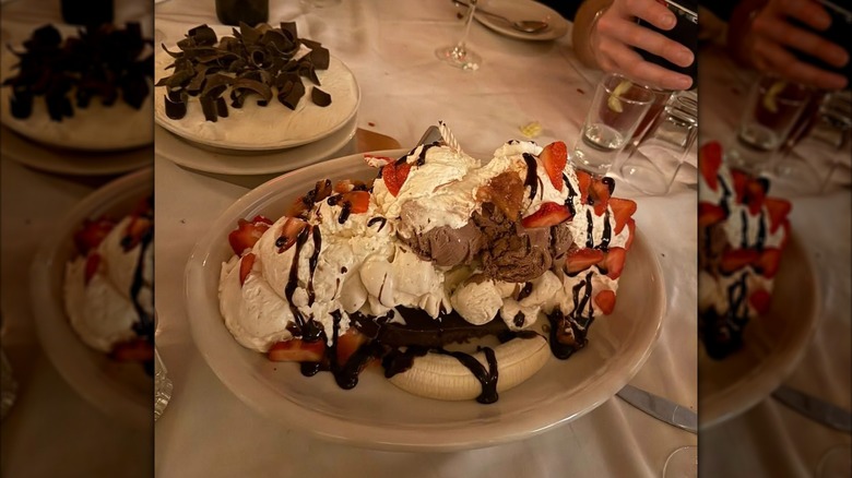 An ice cream dessert with banana, strawberries, whipped cream, and hot fudge