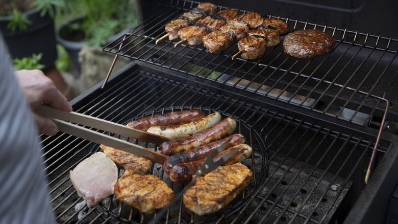 Someone barbecuing meat on a grill with tongs