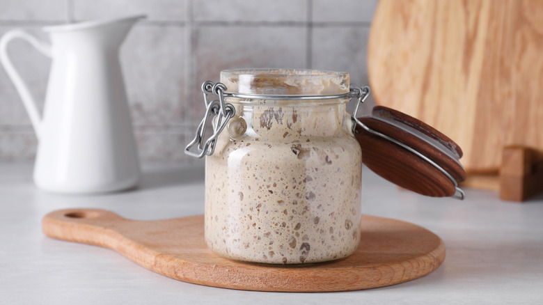 Sourdough starter in a glass jar on a kitchen counter with a white jug in the background