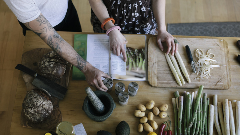 Overhead view of two people cooking asparagus with open cookbook