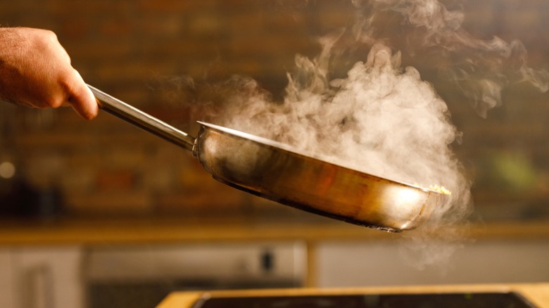 A cook holds a smoking frying pan