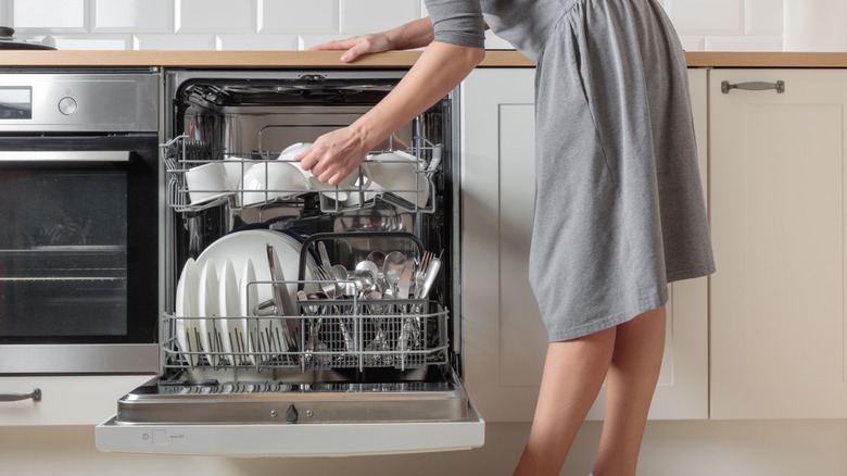 A person in a grey dress opening up a dishwasher.