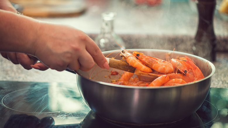 hand holding wooden utensil lifting whole shrimp in metal pot on electric stovetop