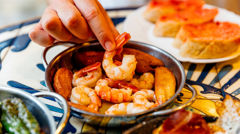 hand picking a cooked shrimp out of a metal bowl next to plate of toasted bread