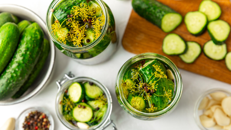Cucumbers rest on a cutting board, in a glass bowl, and pieces sit in three glass jars.