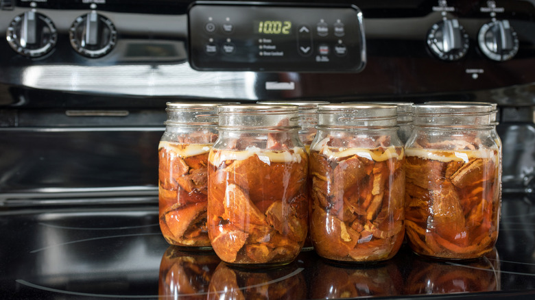 Several jars of canned meat rest on a black stovetop. There are dials and oven clock in the background.