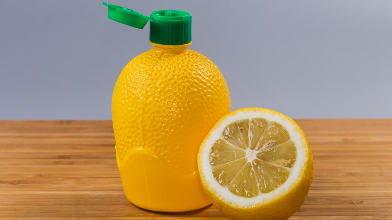 A lemon and lemon juice bottle rest on a wooden table.