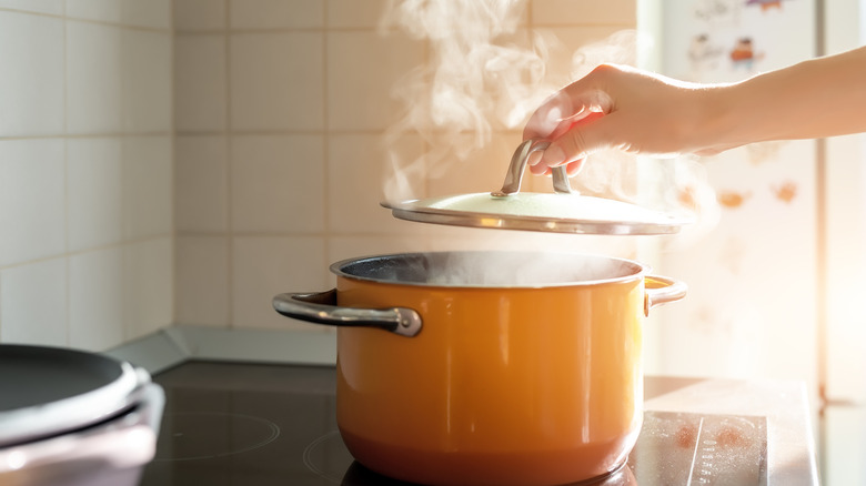Hand lifting lid off steaming pot