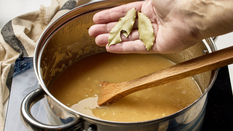 A hand adding two bay leaves to a pot of soup