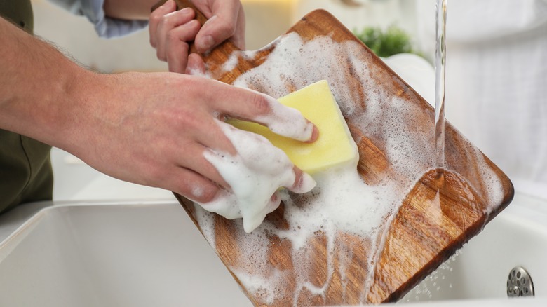 Man washing wooden cutting board in kitchen, closeup