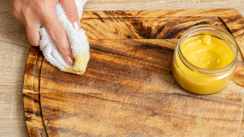 Woman hands apply homemade beeswax wood treatment polish to restore natural wood cutting board.