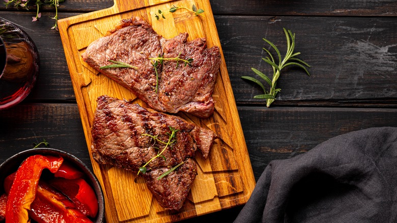 Grilled beef steak, well done with seasons and a glass of red wine on a black wooden background and cutting board top view