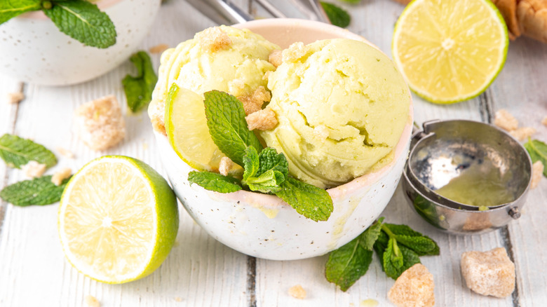 A bowl of ice cream styled with cut limes and fresh mint on a wood table
