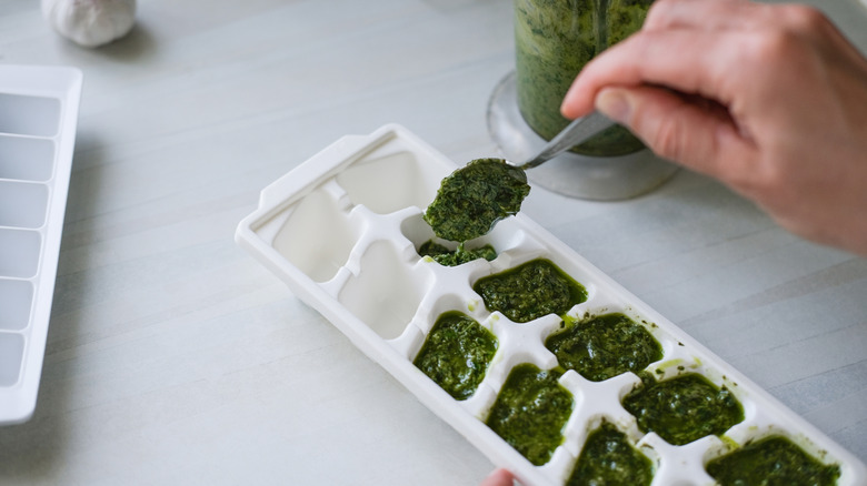 A hand spooning fresh herbs into an ice cube tray