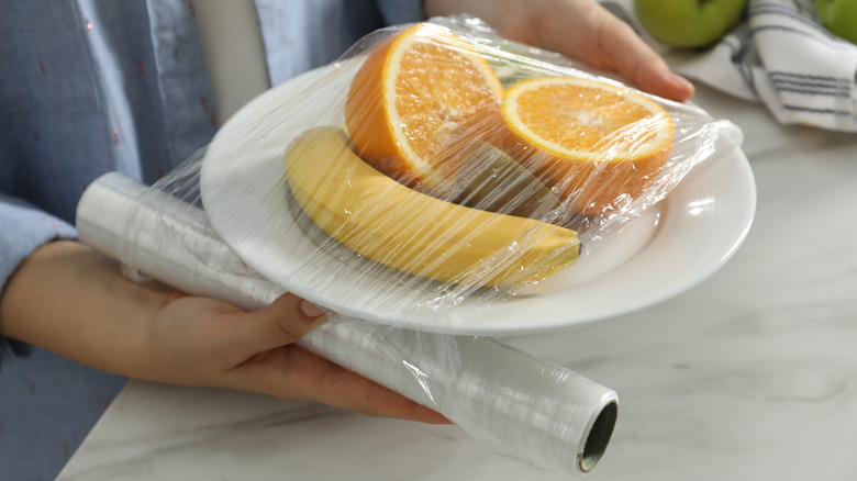 A plate of fruit being covered with plastic wrap
