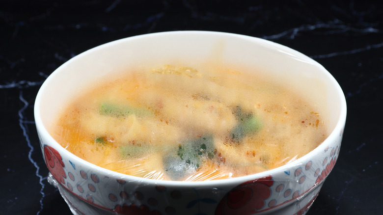 A bowl of microwaved food on a black counter, with plastic wrap covering the top
