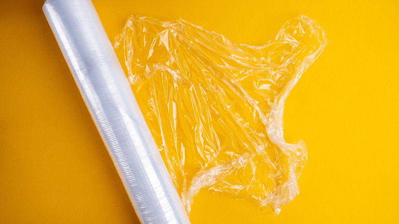 A roll of plastic wrap, partially unrolled on a yellow background