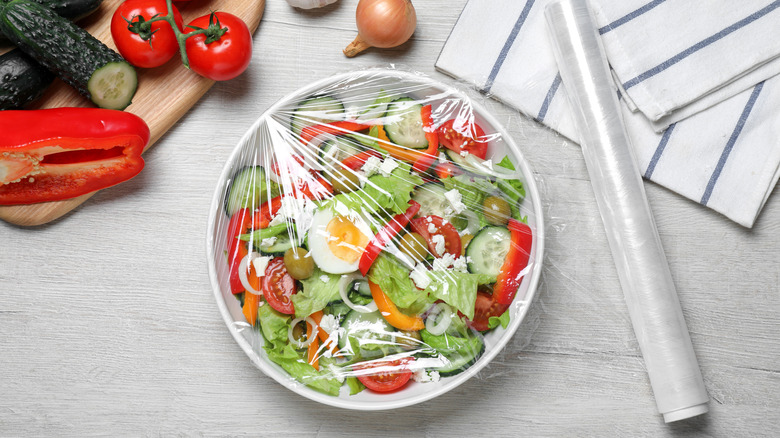 Plastic wrap covering a bowl of salad, with a roll of plastic wrap next to it