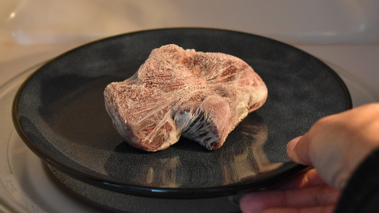 A piece of frozen meat on a black plate, wrapped in plastic wrap