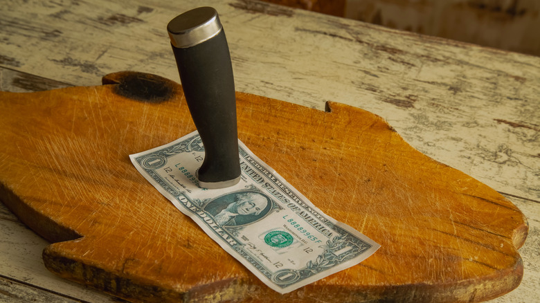knife handle pinning one dollar bill to fish shaped cutting board