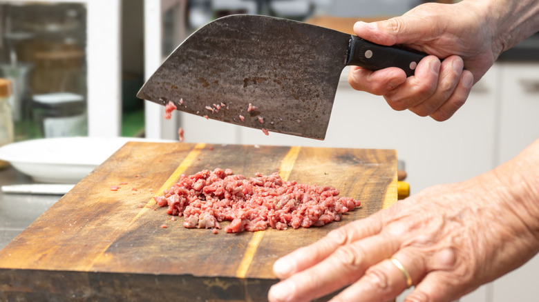 person chopping meat on a wooden butcher block