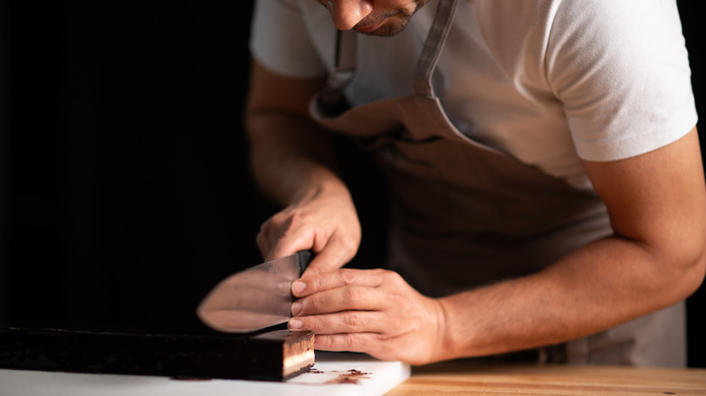 man in apron using knife to slice food