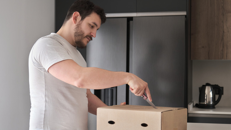 man using kitchen knife to open box