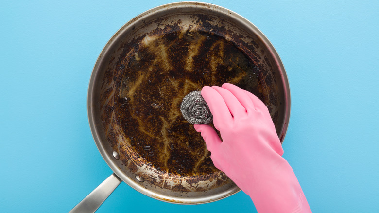 hand wearing pink glove washing pan with steel wool